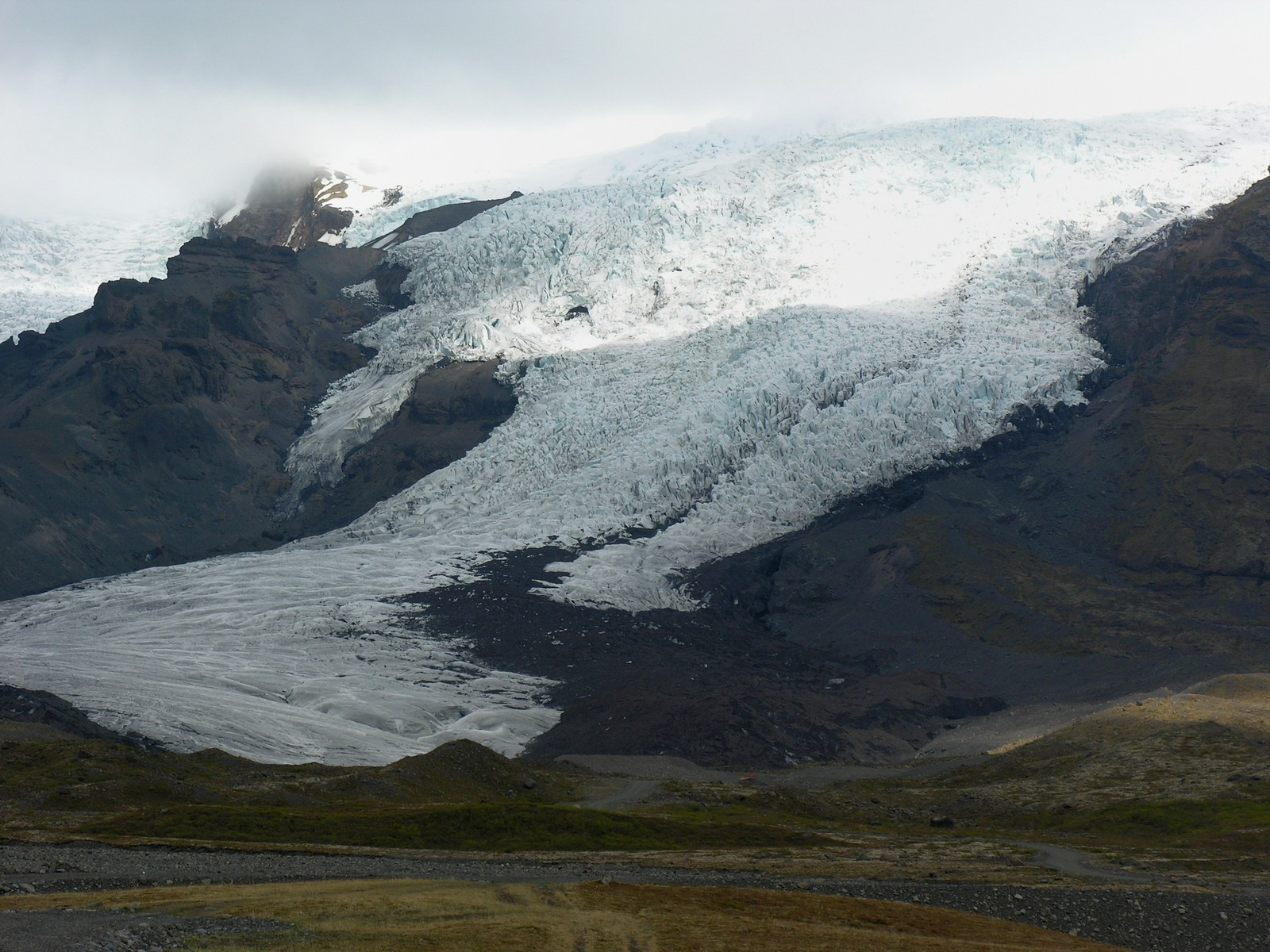 The crevassed ice of Falljökull glacier descends between dark mountains in Vatnajökull National Park, Iceland.