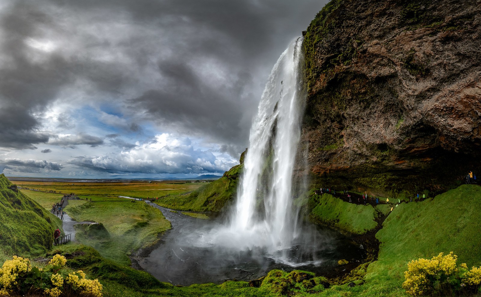 Seljalandsfoss plunges beside a green cliff in southern Iceland, with the walking path passing behind the waterfall.